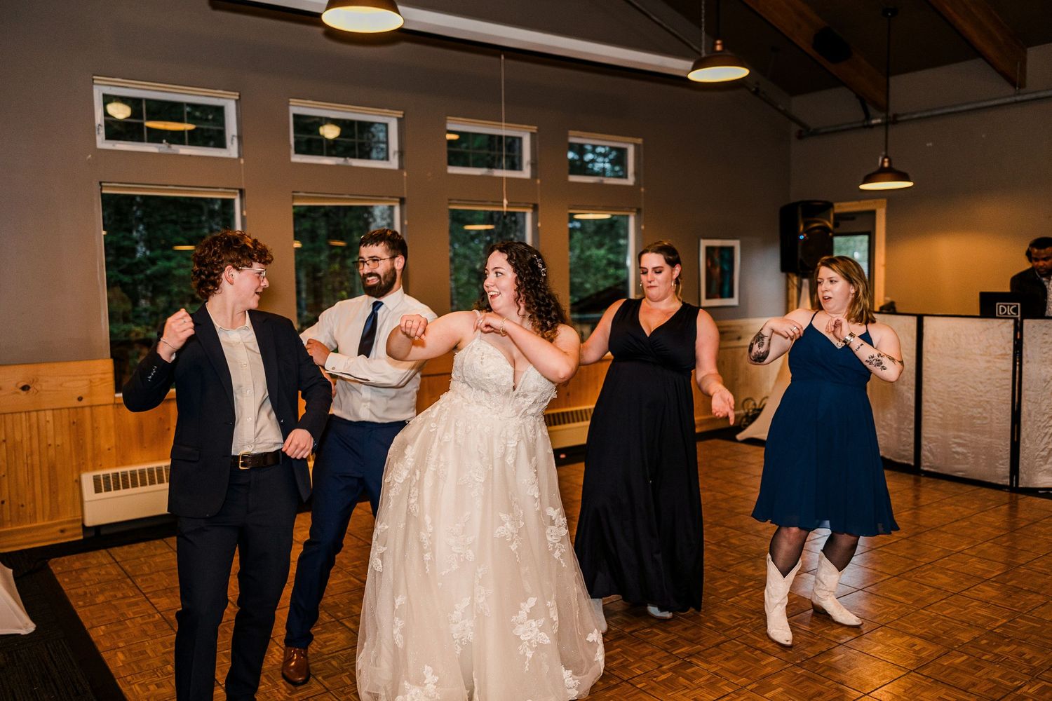 Wedding party dancing together on a wooden dance floor during reception celebrations.