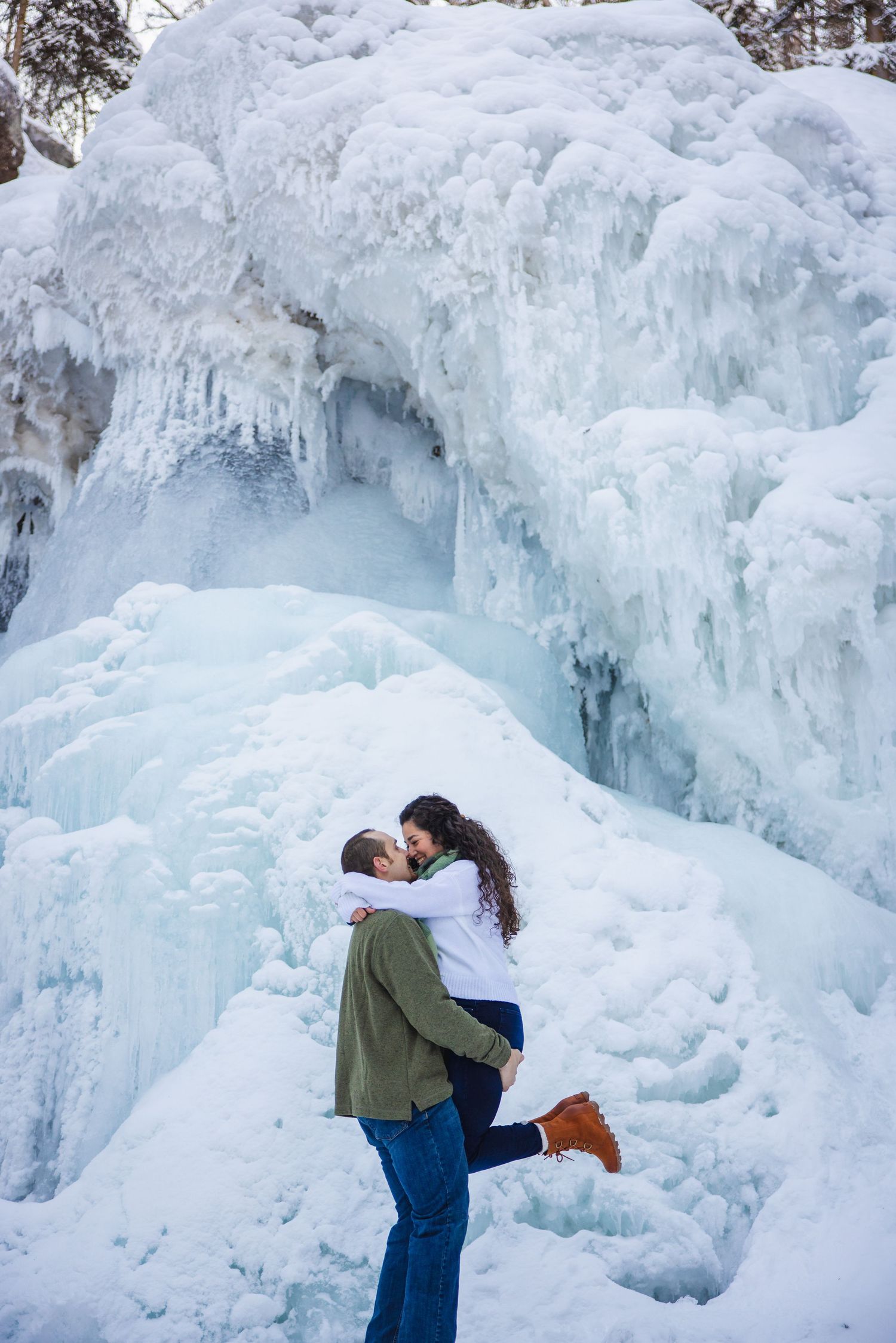 Couple kissing in front of a massive frozen waterfall covered in blue ice and icicles.