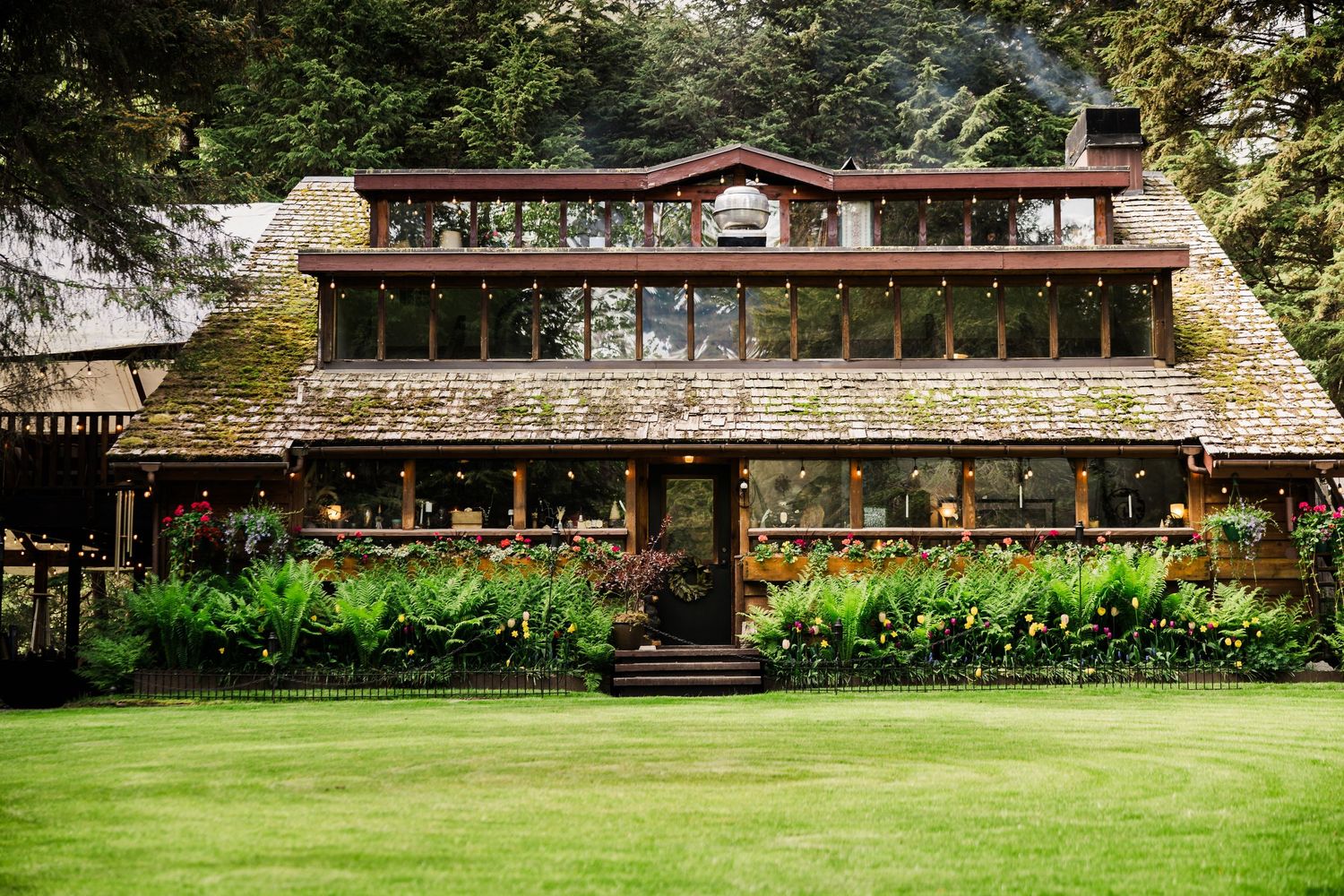 Rustic lodge venue with moss-covered roof and flower gardens in Pacific Northwest setting.