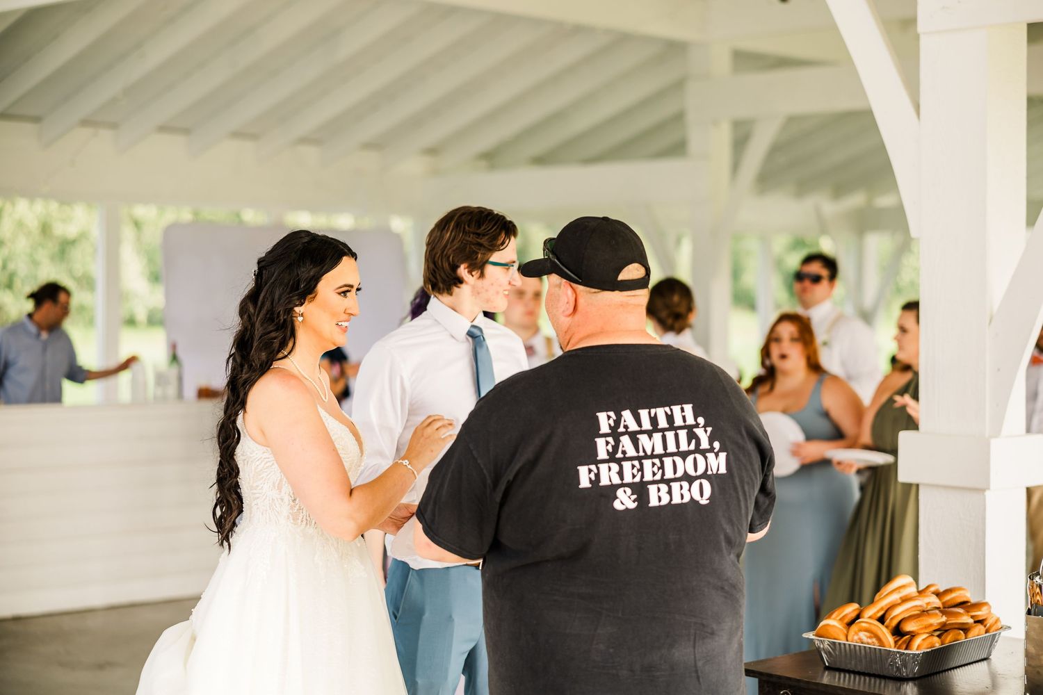Wedding reception scene with catering staff and guests mingling under white pavilion.