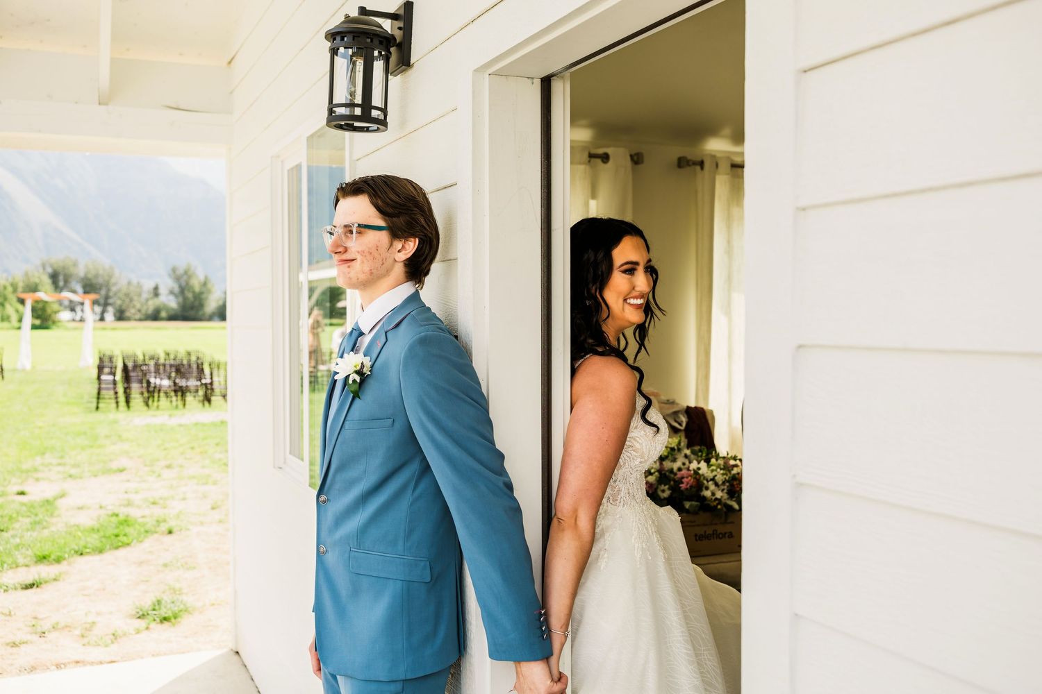 Bride and groom sharing a sweet first look moment standing back to back at barn venue.