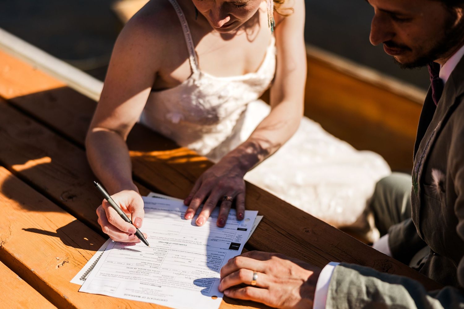 Signing wedding documents at wooden table in outdoor setting.