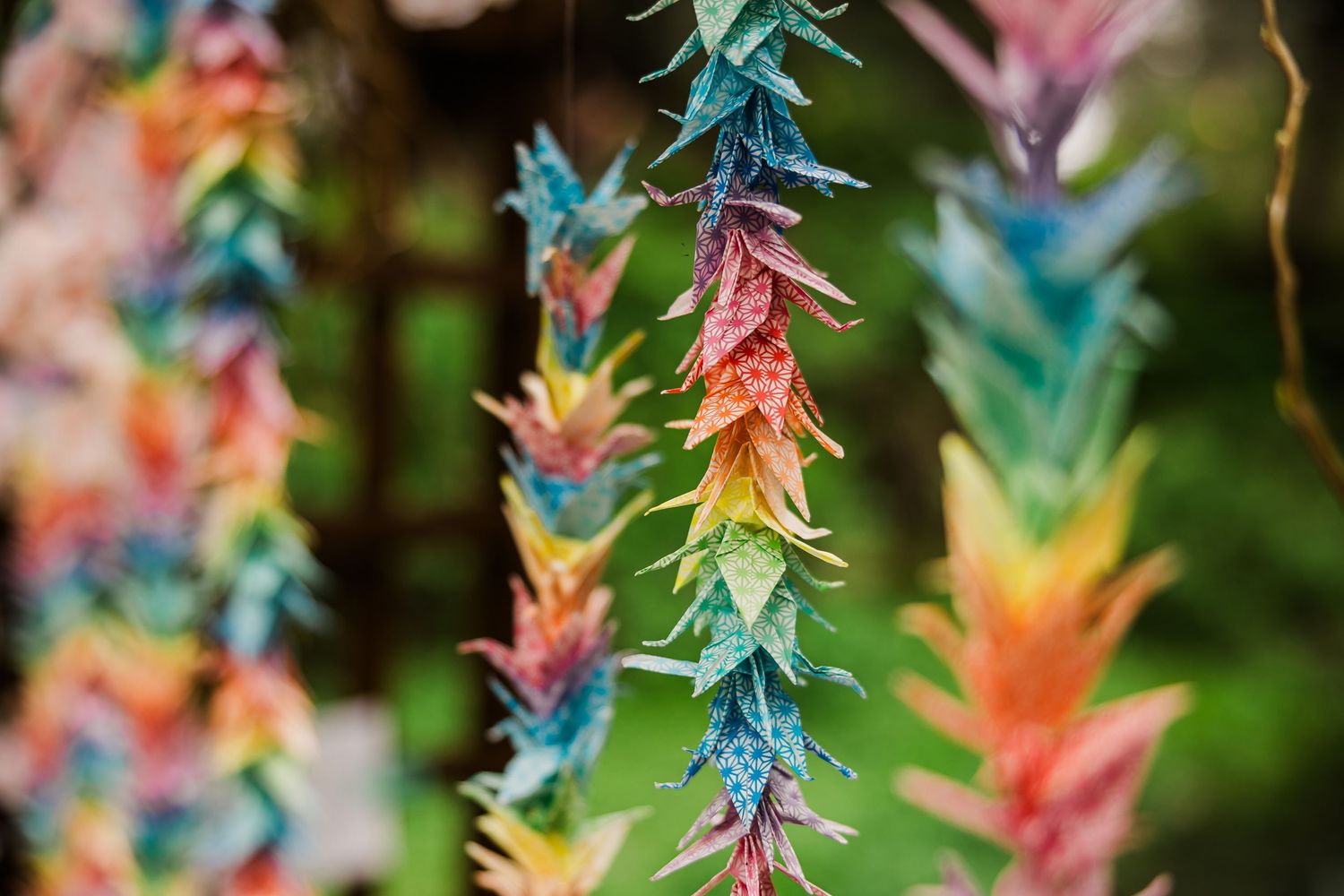 Colorful paper origami garland hangs with vibrant rainbow hues against green background.