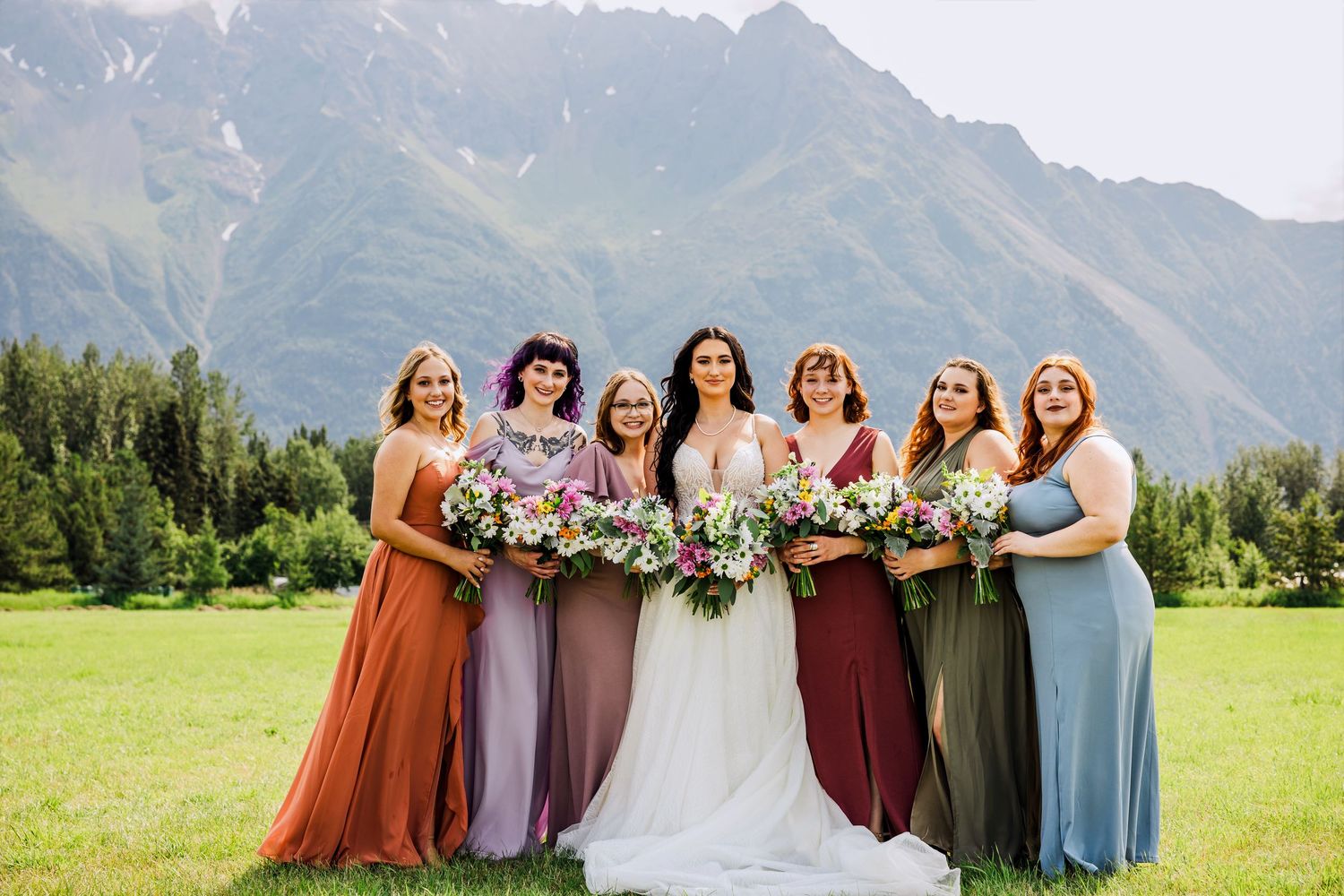 Wedding party in colorful dresses poses together with mountain scenery.