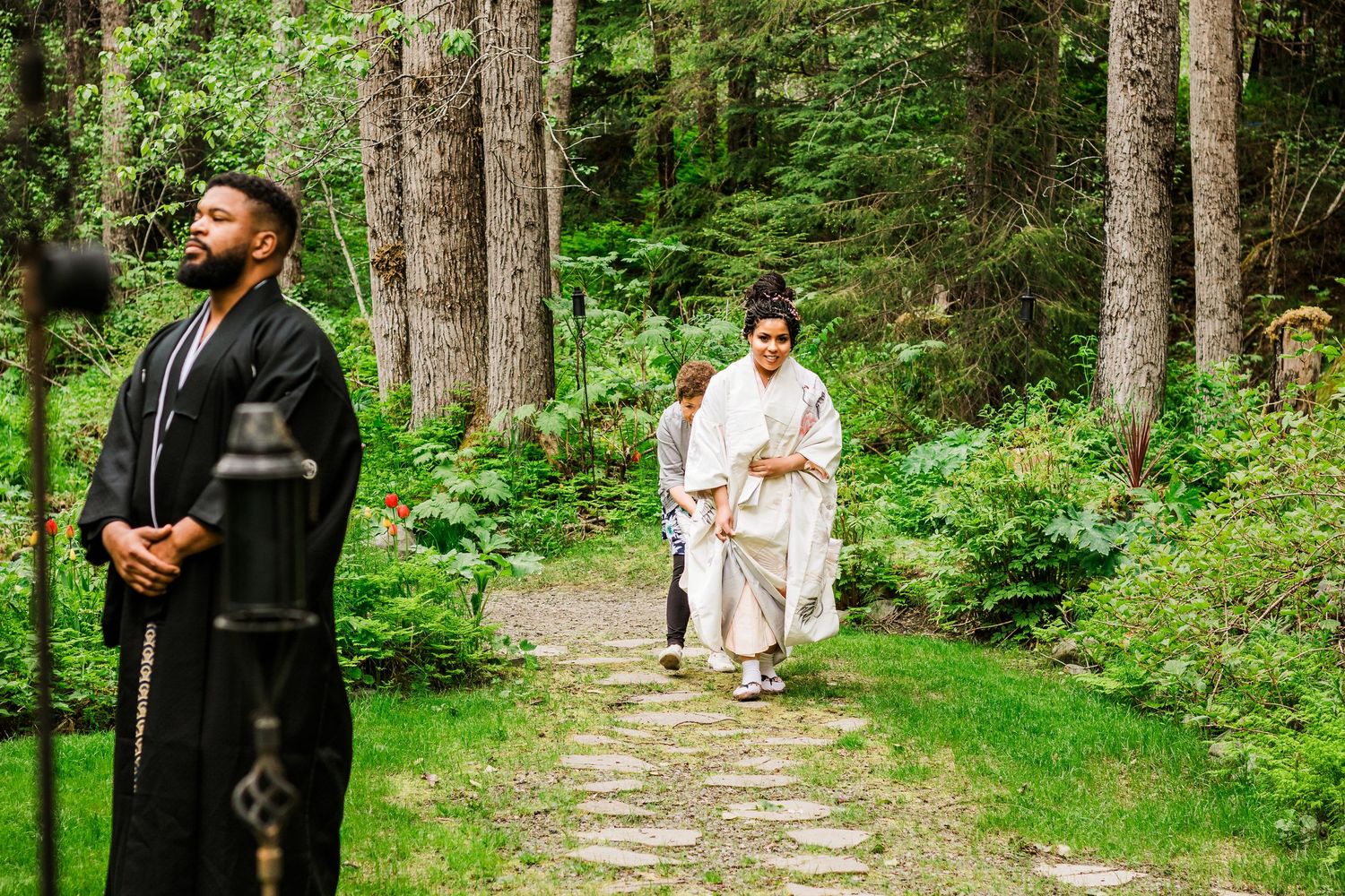 Couple has traditional Japanese wedding ceremony on forest path with officiant in black robe.