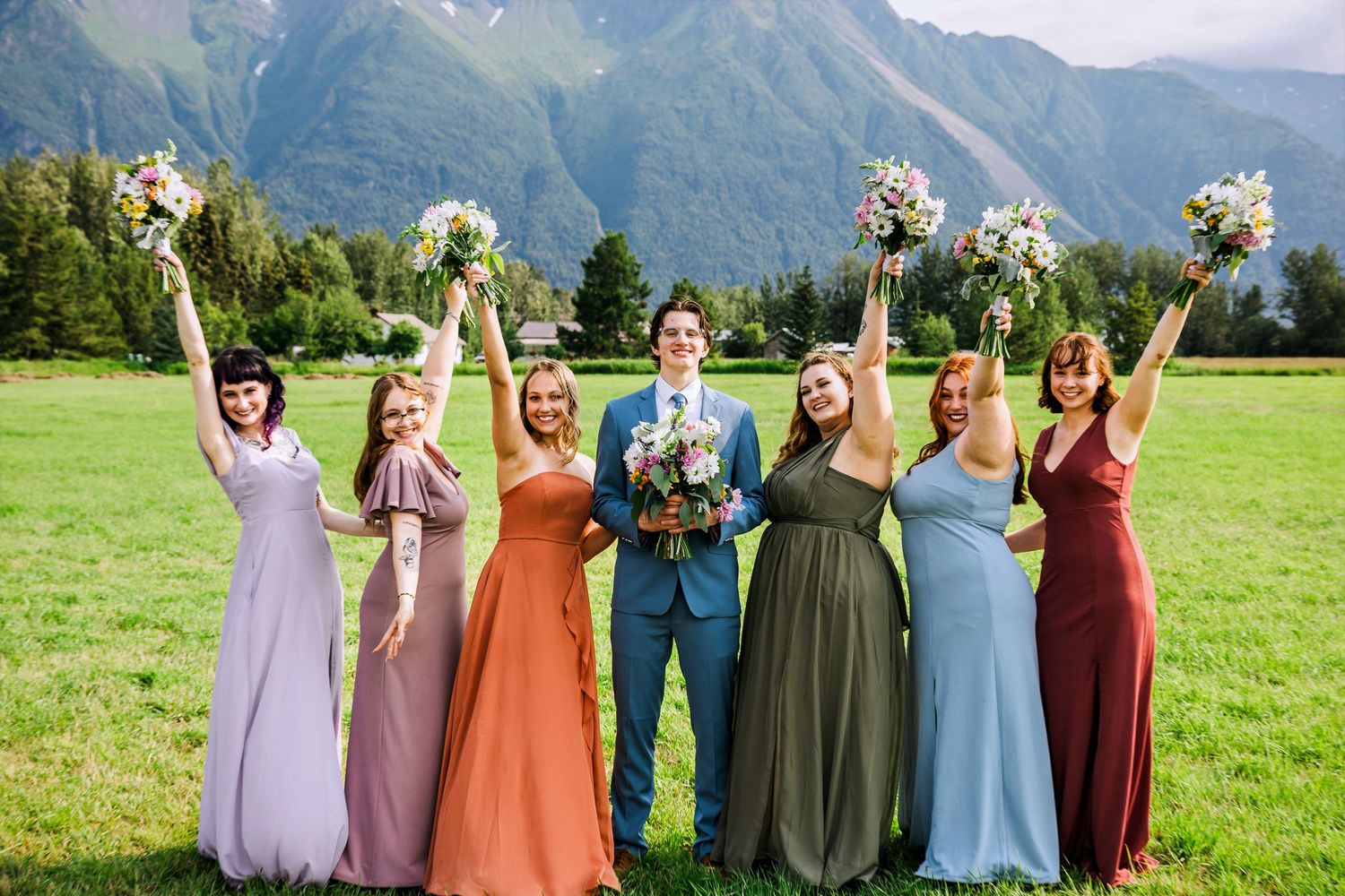 Wedding party in colorful dresses poses with bouquets against scenic mountain vista.