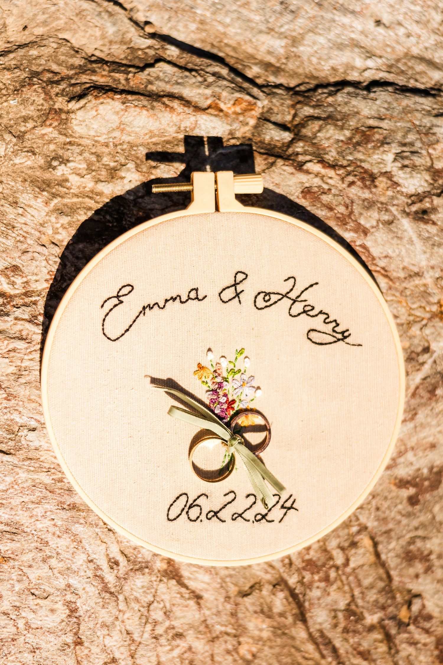 Embroidered wedding hoop with date and floral design against textured stone background.