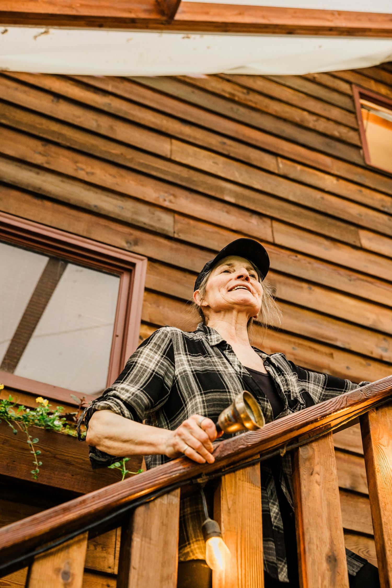 Person in plaid shirt standing on wooden cabin balcony looking into distance.