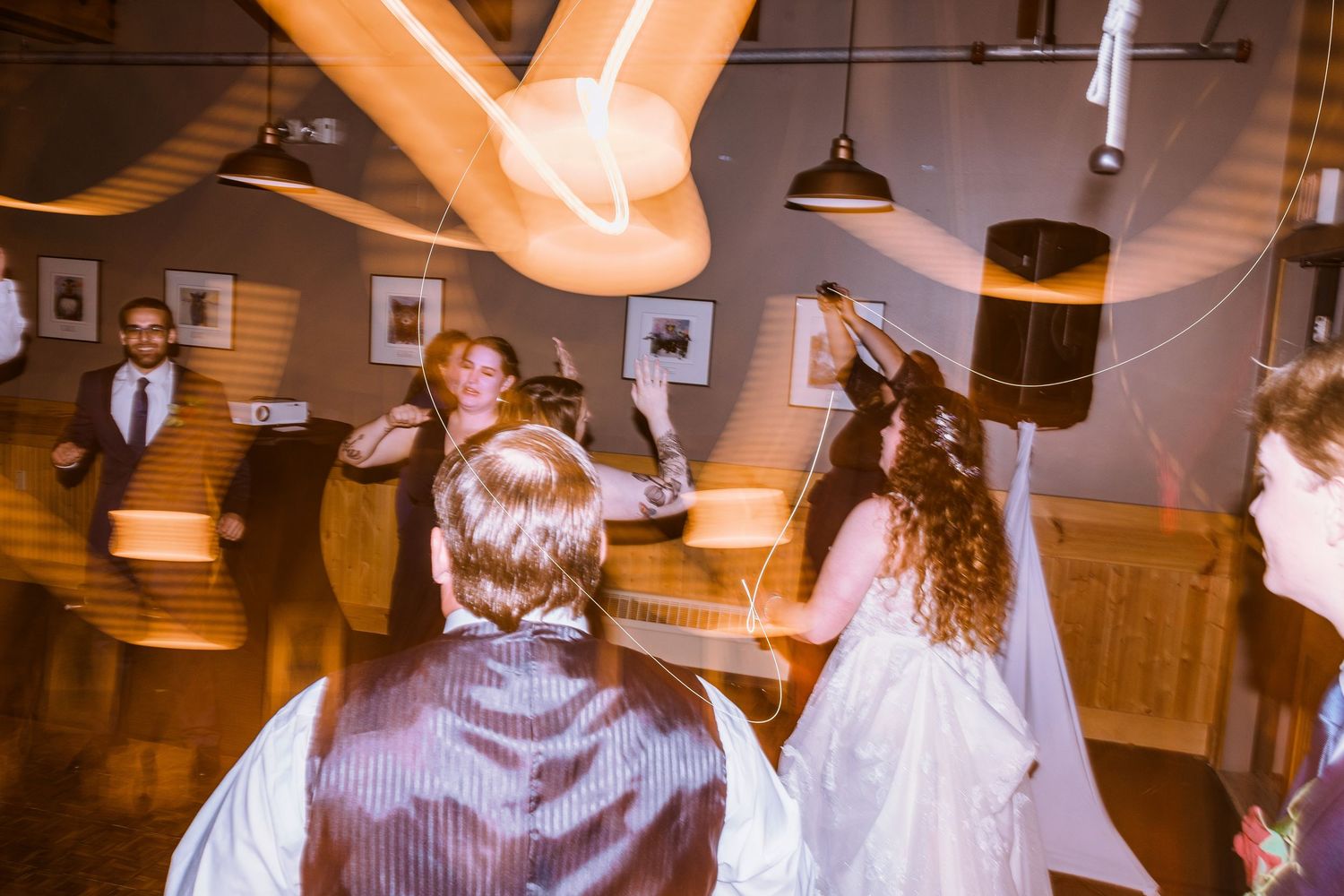 Wedding guests dancing and celebrating at an indoor reception venue with warm lighting.
