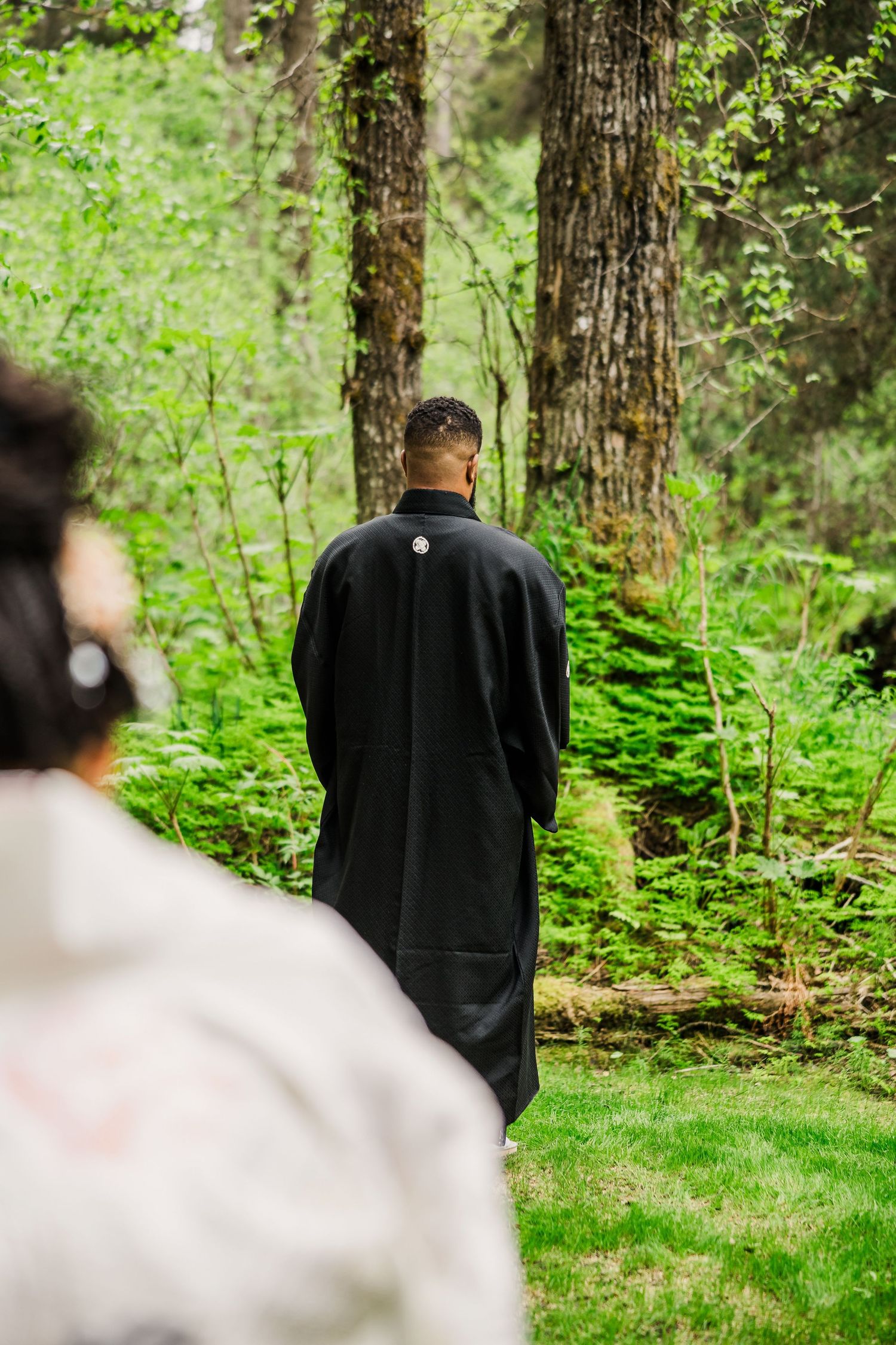 Back view of officiant in black robe during outdoor forest wedding ceremony.