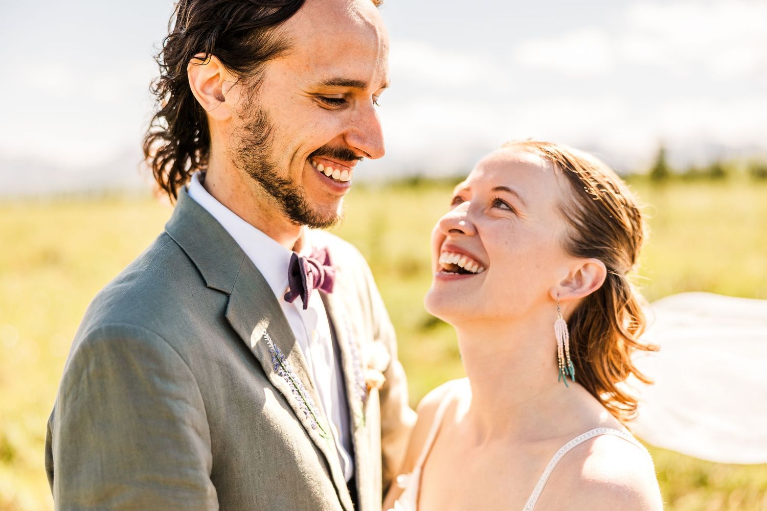 Happy couple shares joyful laughter in sunlit field on their wedding day.