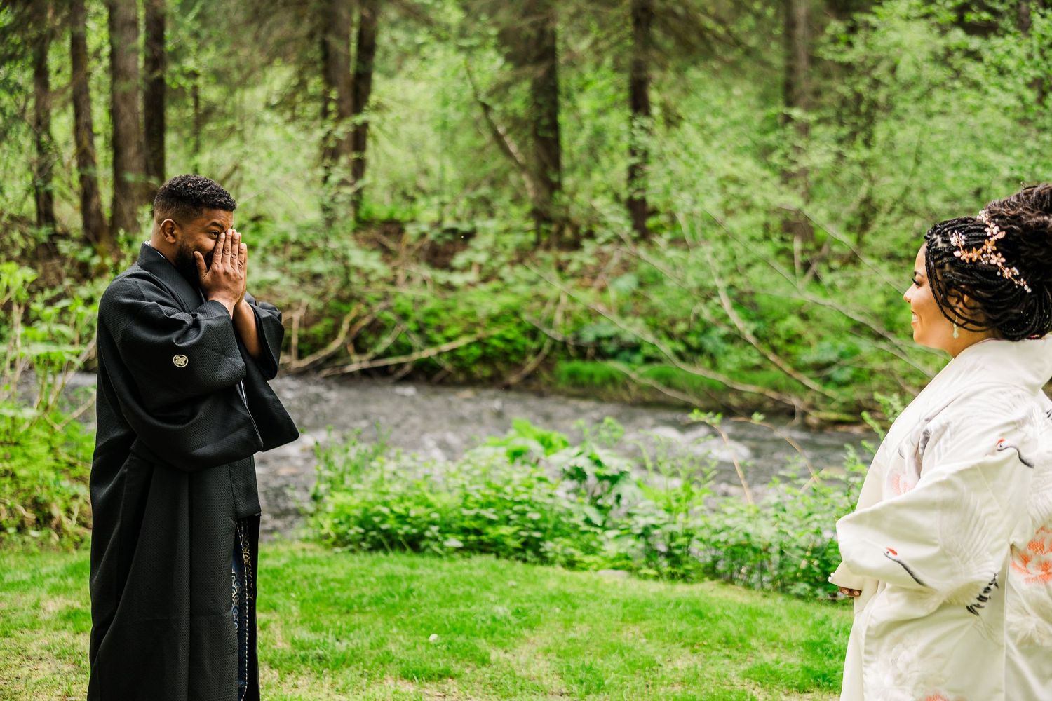 Couple exchanging vows during outdoor wedding ceremony by stream in lush forest.
