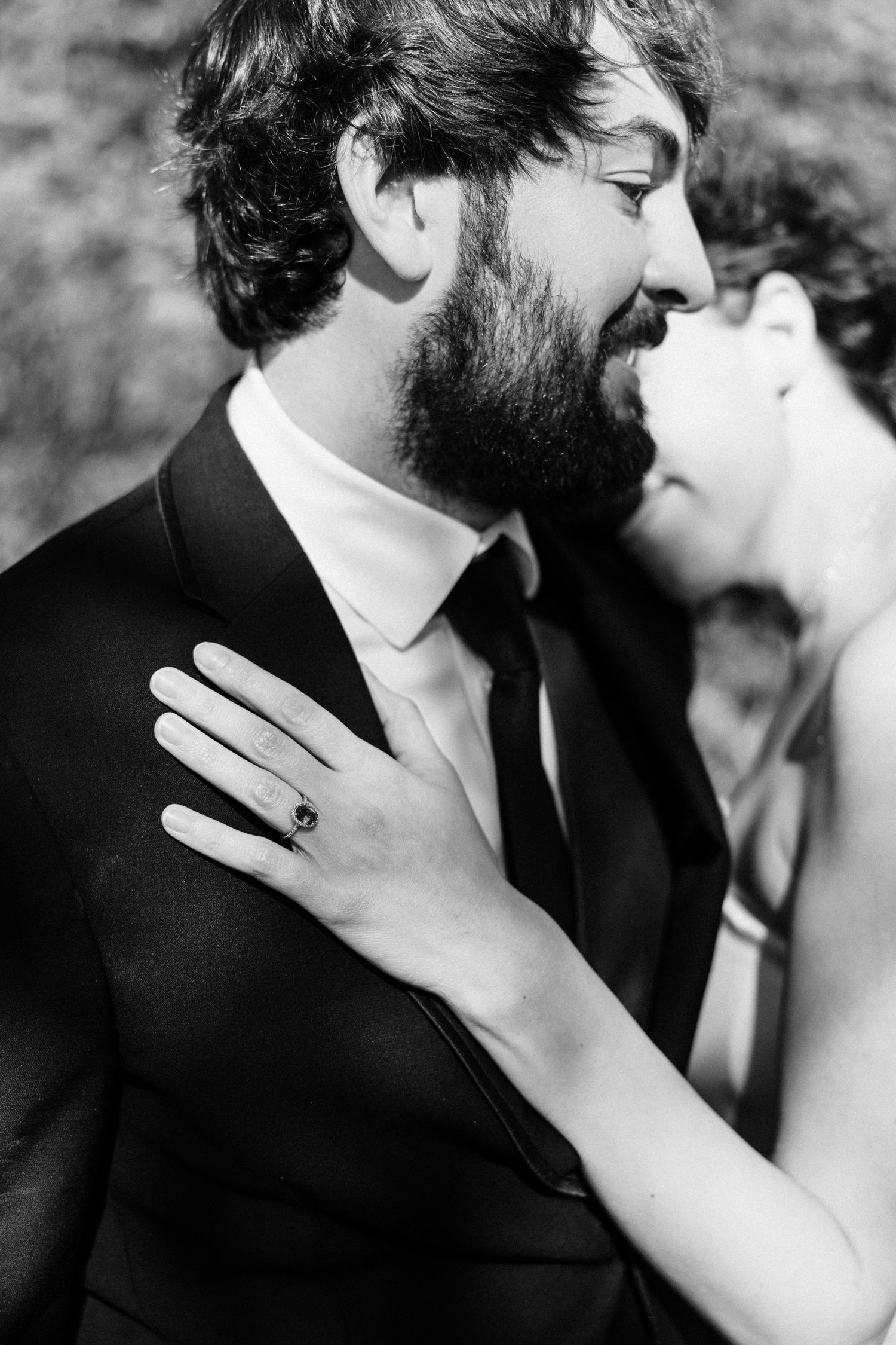 Black and white close-up of bride resting hand with engagement ring on grooms suit jacket.
