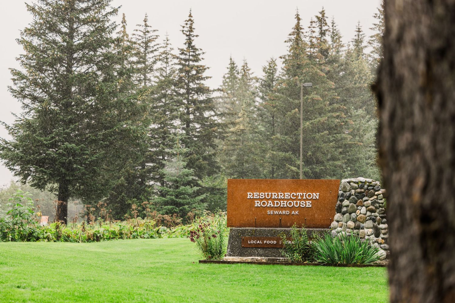 Breitenbush Retreat wooden entrance sign surrounded by evergreen trees and garden landscaping.