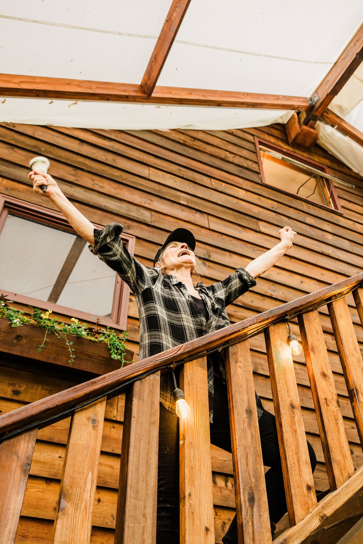 Person in plaid shirt celebrating with arms raised on rustic wooden cabin deck.
