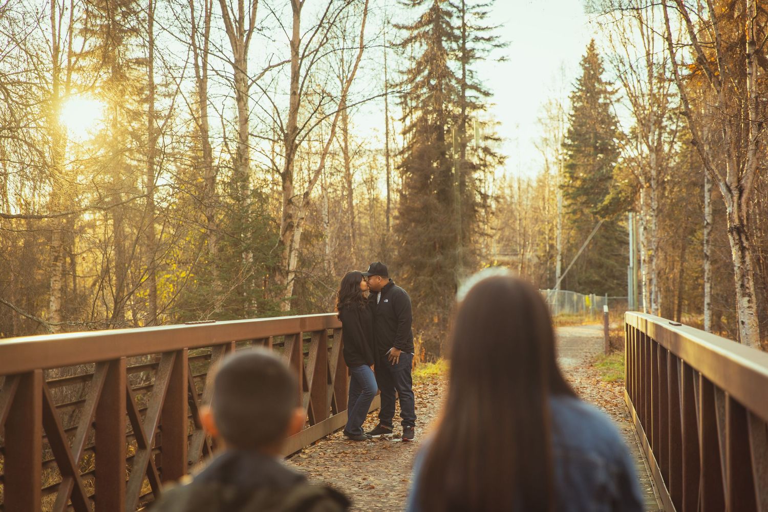 Family walking on a wooden bridge surrounded by autumn trees at golden hour sunset.