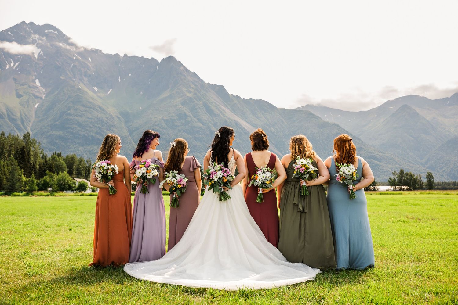 Wedding party in earth-toned dresses stand against dramatic mountain landscape.
