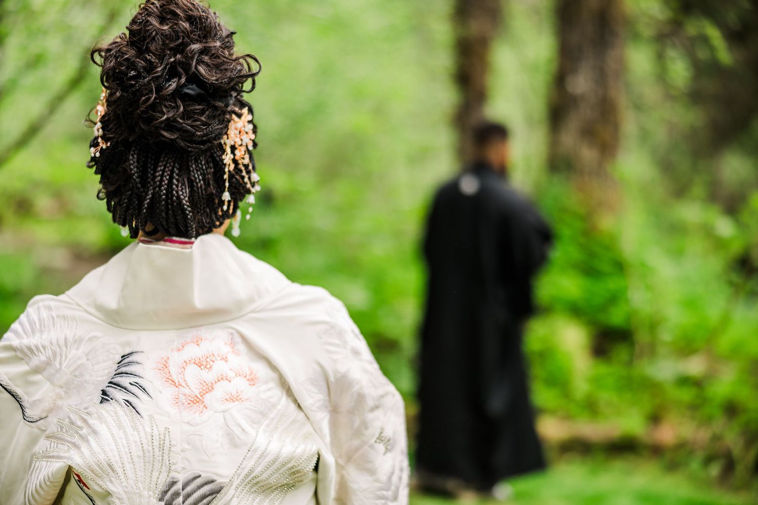 Back view of bride in white kimono looking at groom during forest ceremony.