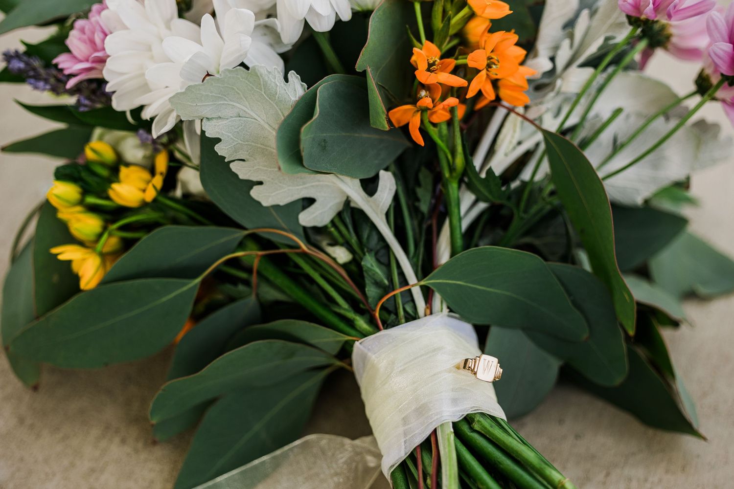 Elegant wedding bouquet with white flowers, greenery, and pops of yellow and orange blooms.