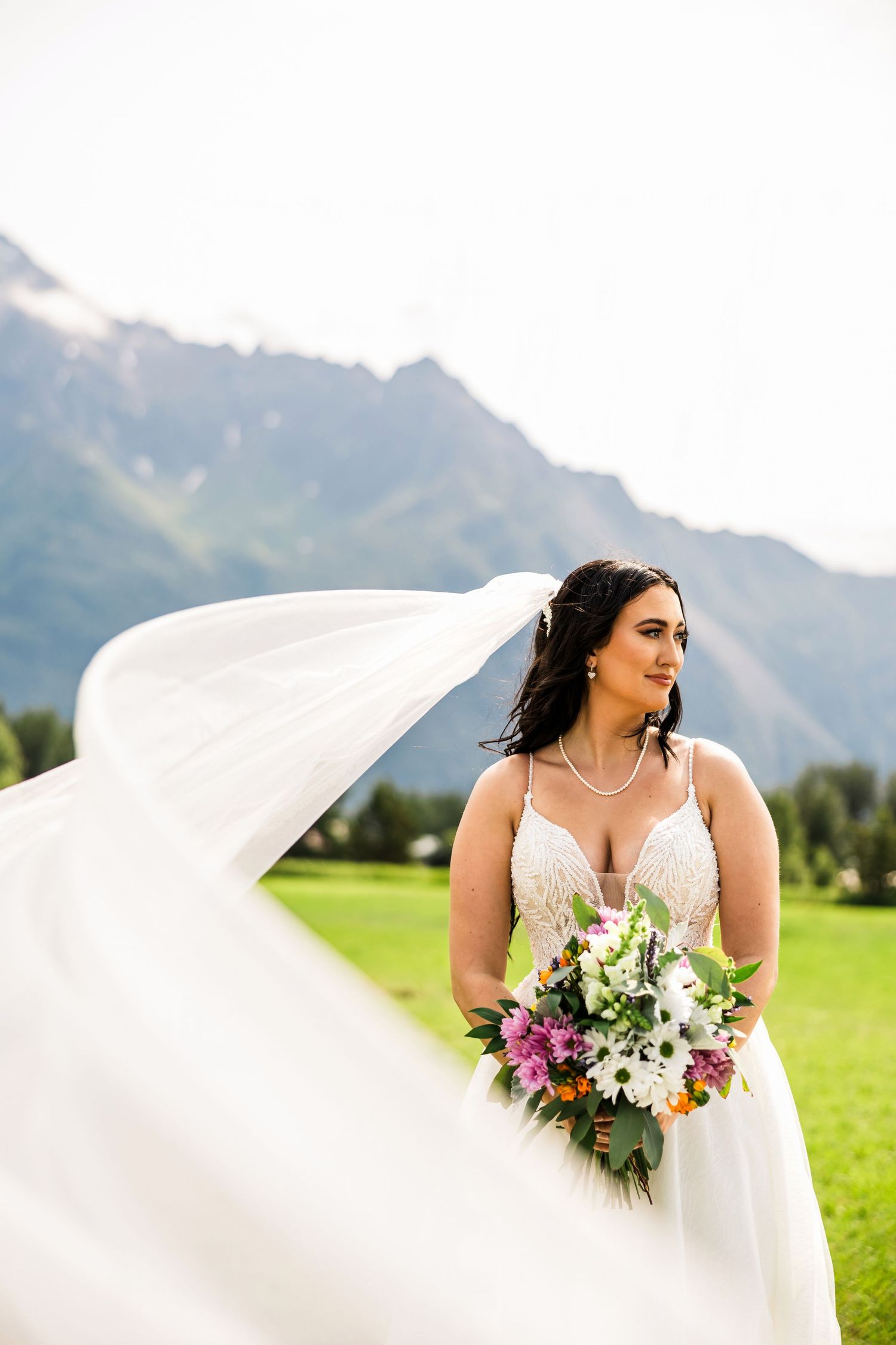 A white wedding dress billows dramatically in the breeze against a stunning mountain backdrop.