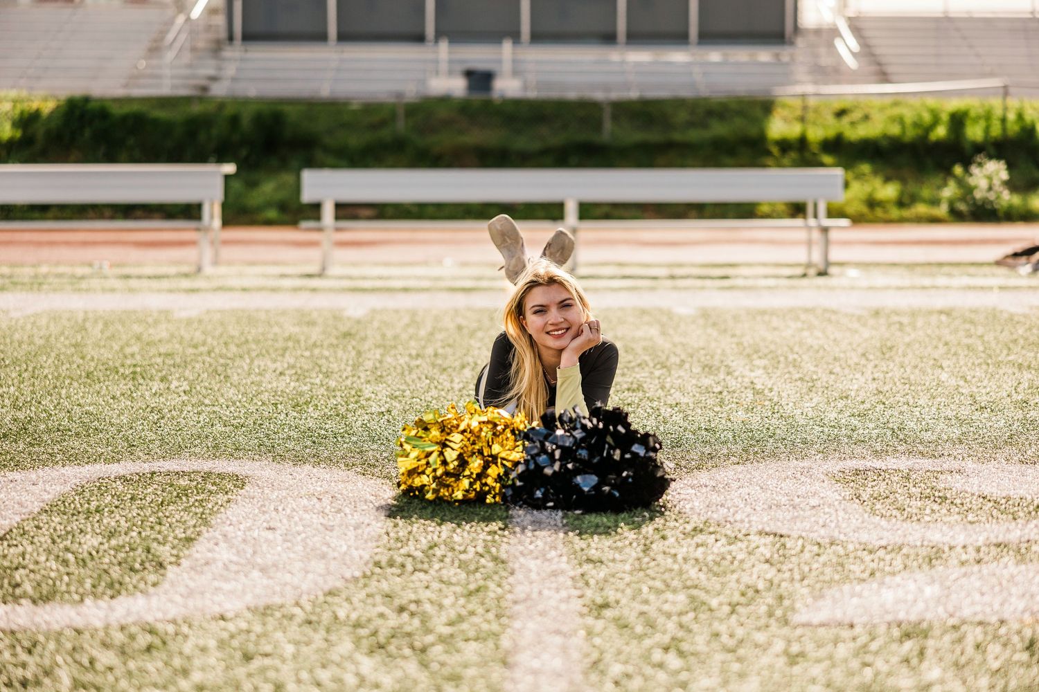 Cheerleader in bunny ears lies on a football field surrounded by yellow and black pom-poms.