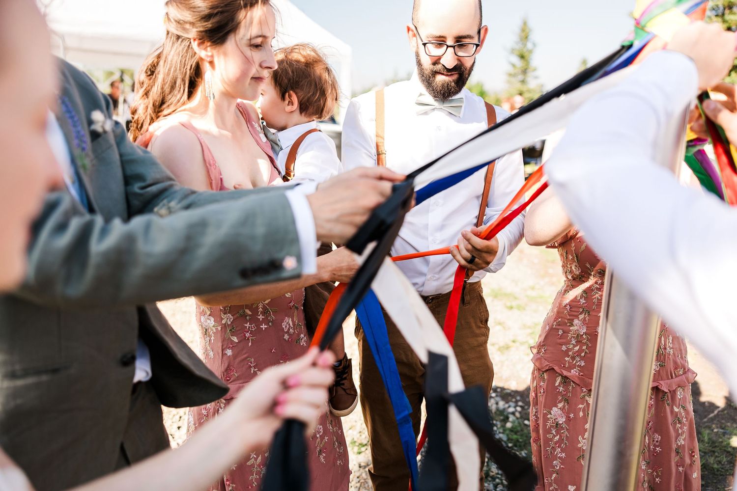 Wedding guests hold colorful ribbons during an outdoor ceremony.