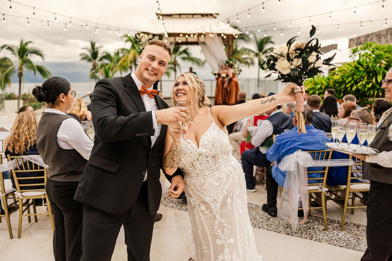 Joyful bride and groom celebrating at outdoor tropical wedding reception with guests.