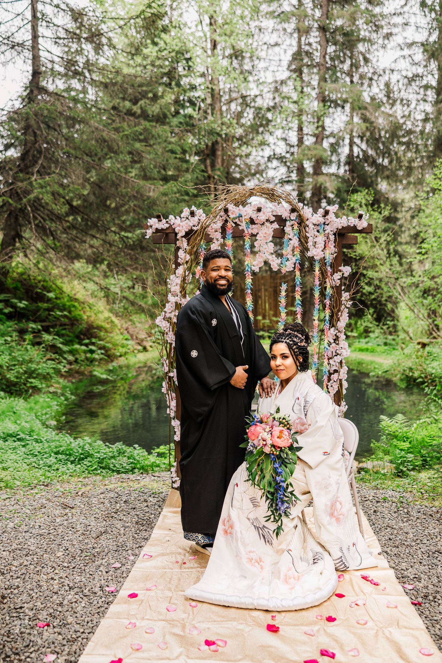 Traditional wedding attire portrait under a floral arch with rose petals scattered on the ground.