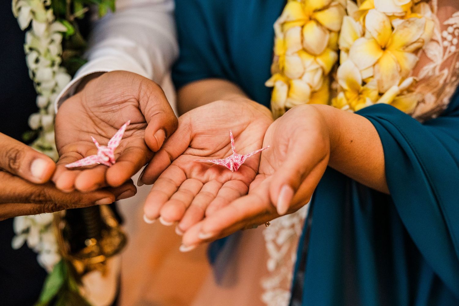 Close-up of hands holding delicate rings during a wedding ceremony with floral decorations.