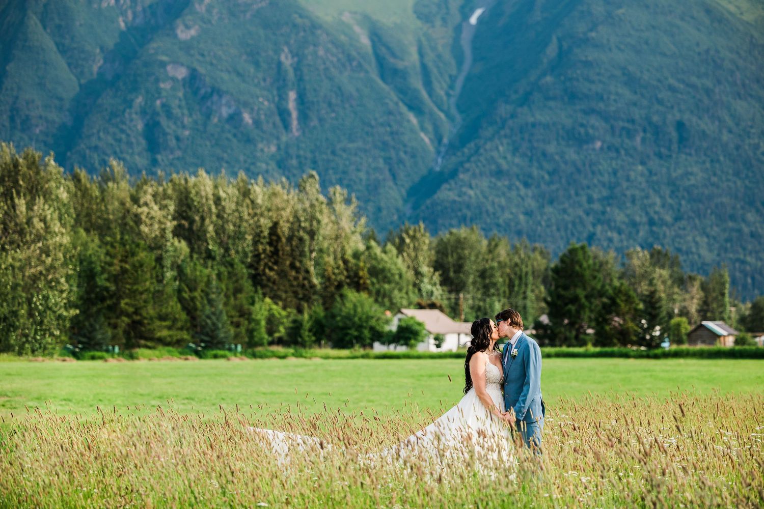 Couple walking through field with majestic mountains rising in background.
