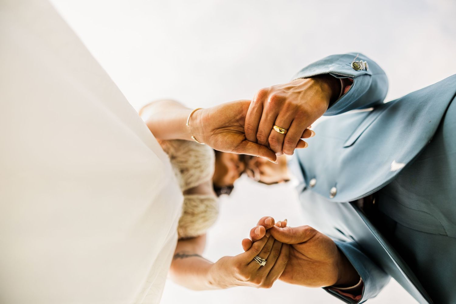 Close-up of joined hands showing wedding rings against light background.