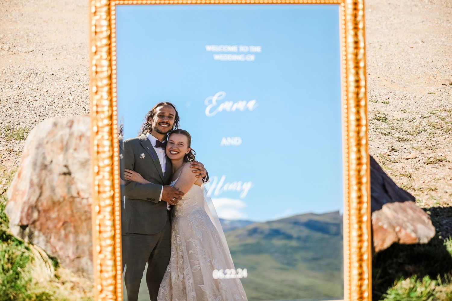 Wedding couple's reflection in decorative gold mirror frame with mountain backdrop.