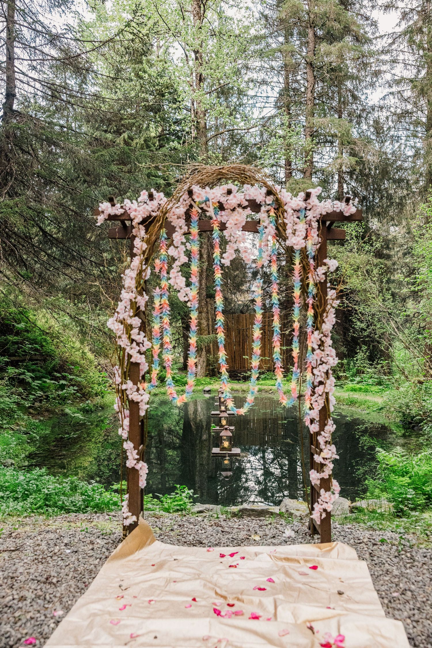 Romantic floral wedding arch decorated with pink blossoms and greenery in a forest setting.