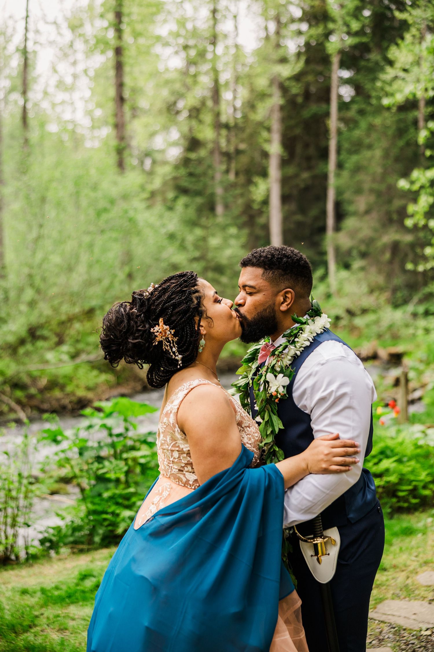 A romantic kiss captured between newlyweds in a verdant forest backdrop.