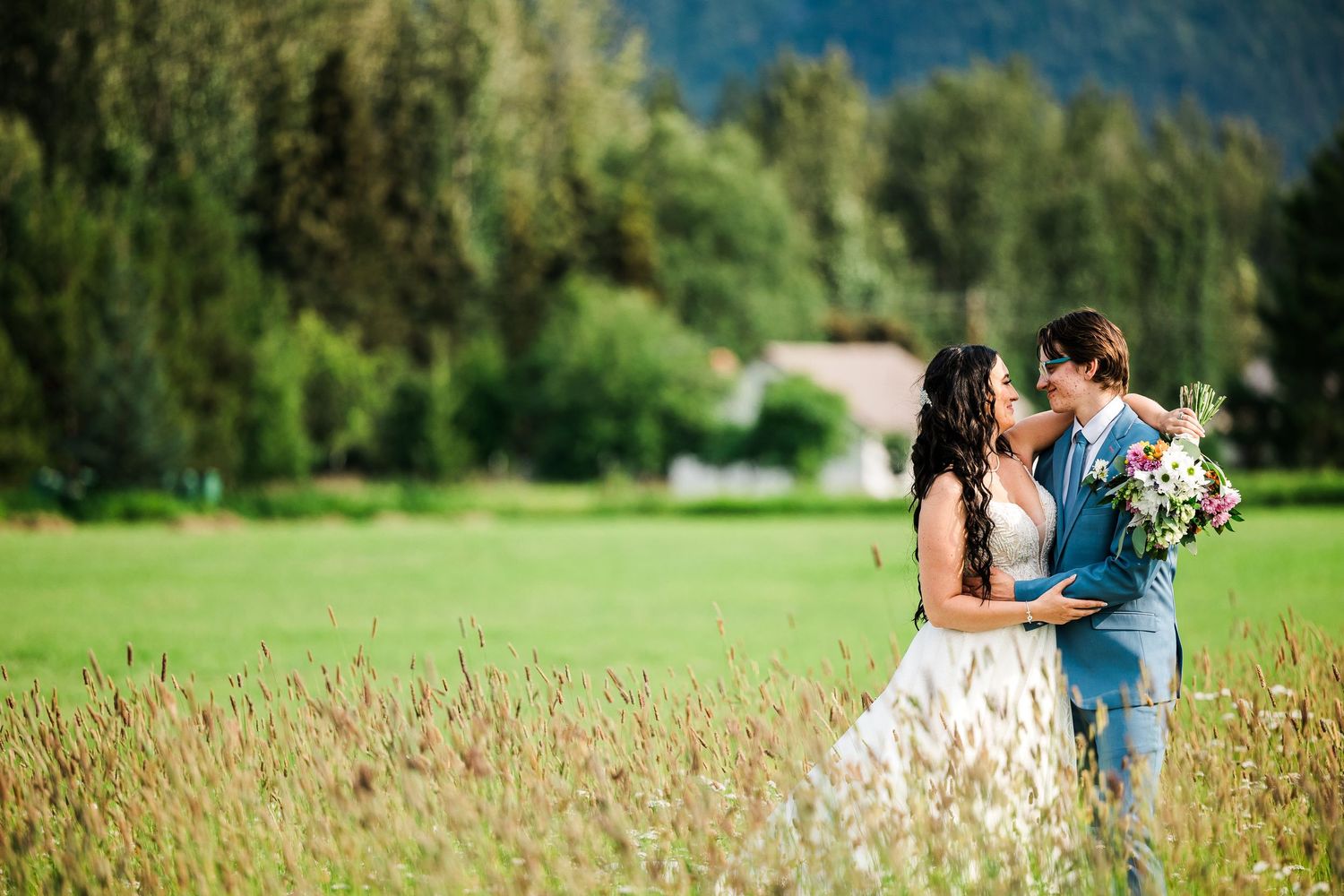 Romantic moment between newlyweds in field with mountains and forest scenery.