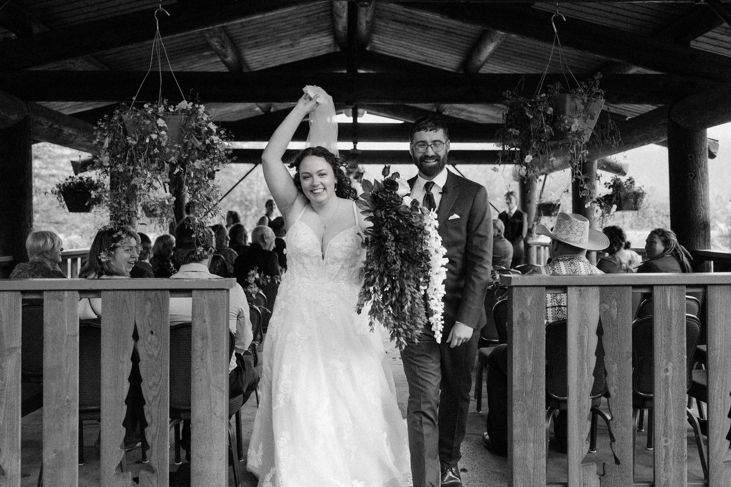 A celebratory wedding moment under a rustic wooden pavilion decorated with greenery and hanging plants.