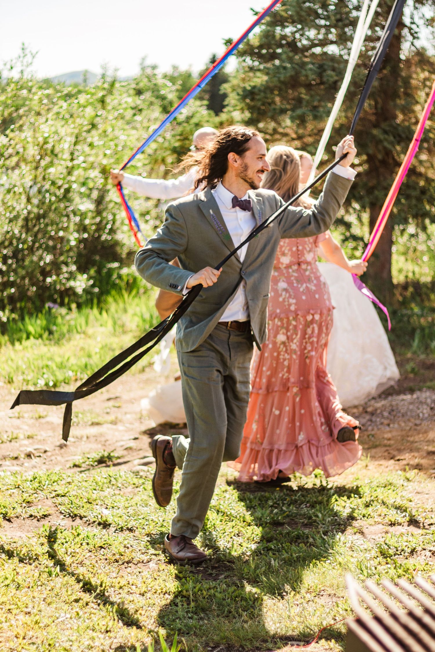 Festive wedding celebration with dancing and colorful ribbons in a mountain setting.