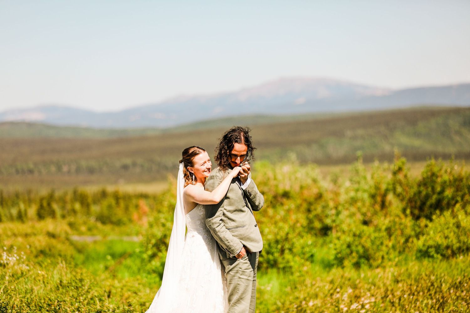 Newlyweds share intimate moment on boardwalk with mountain vista in background.