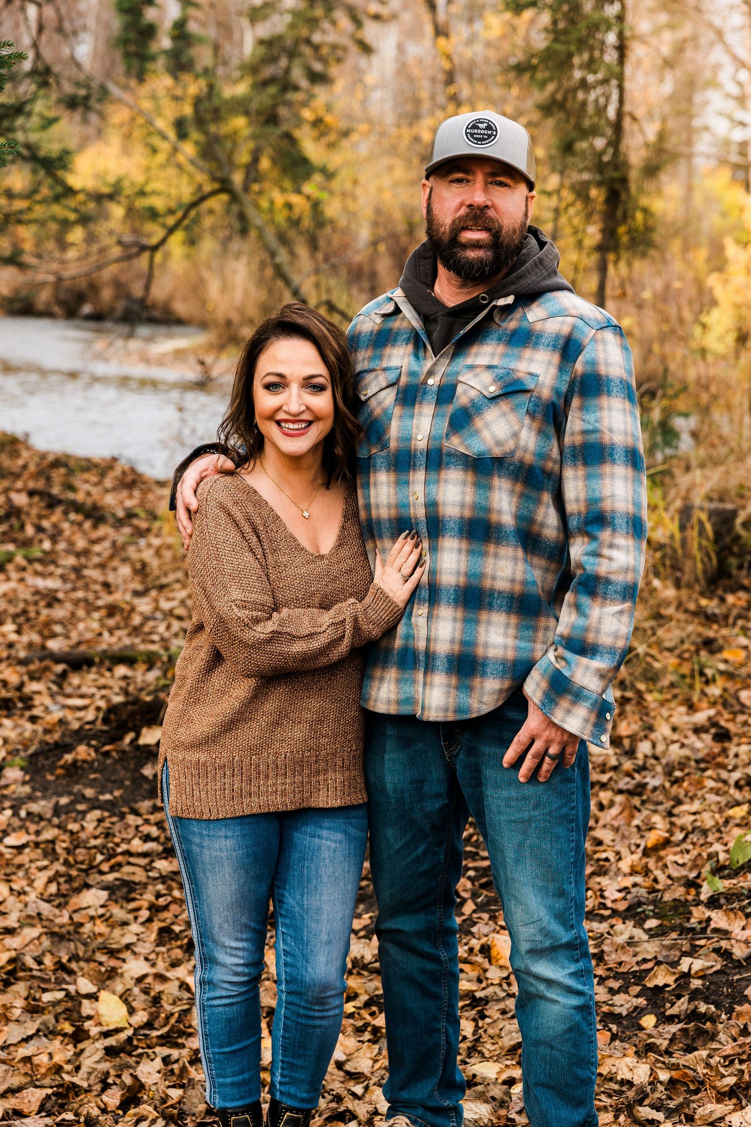 Smiling couple posing together in autumn forest with colorful fallen leaves surrounding them.