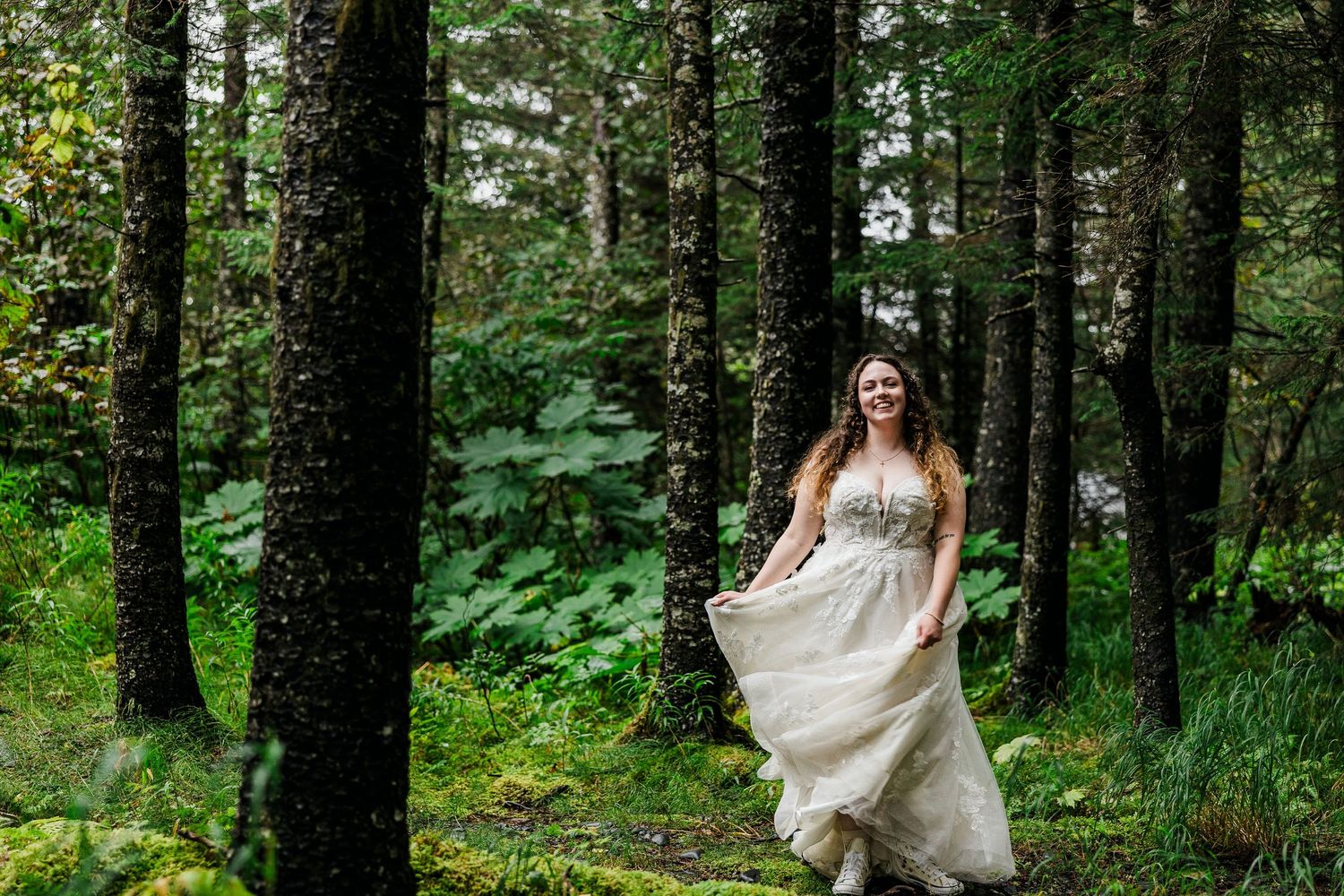 Bride in flowing white dress walks through mossy forest with movement in her skirt.