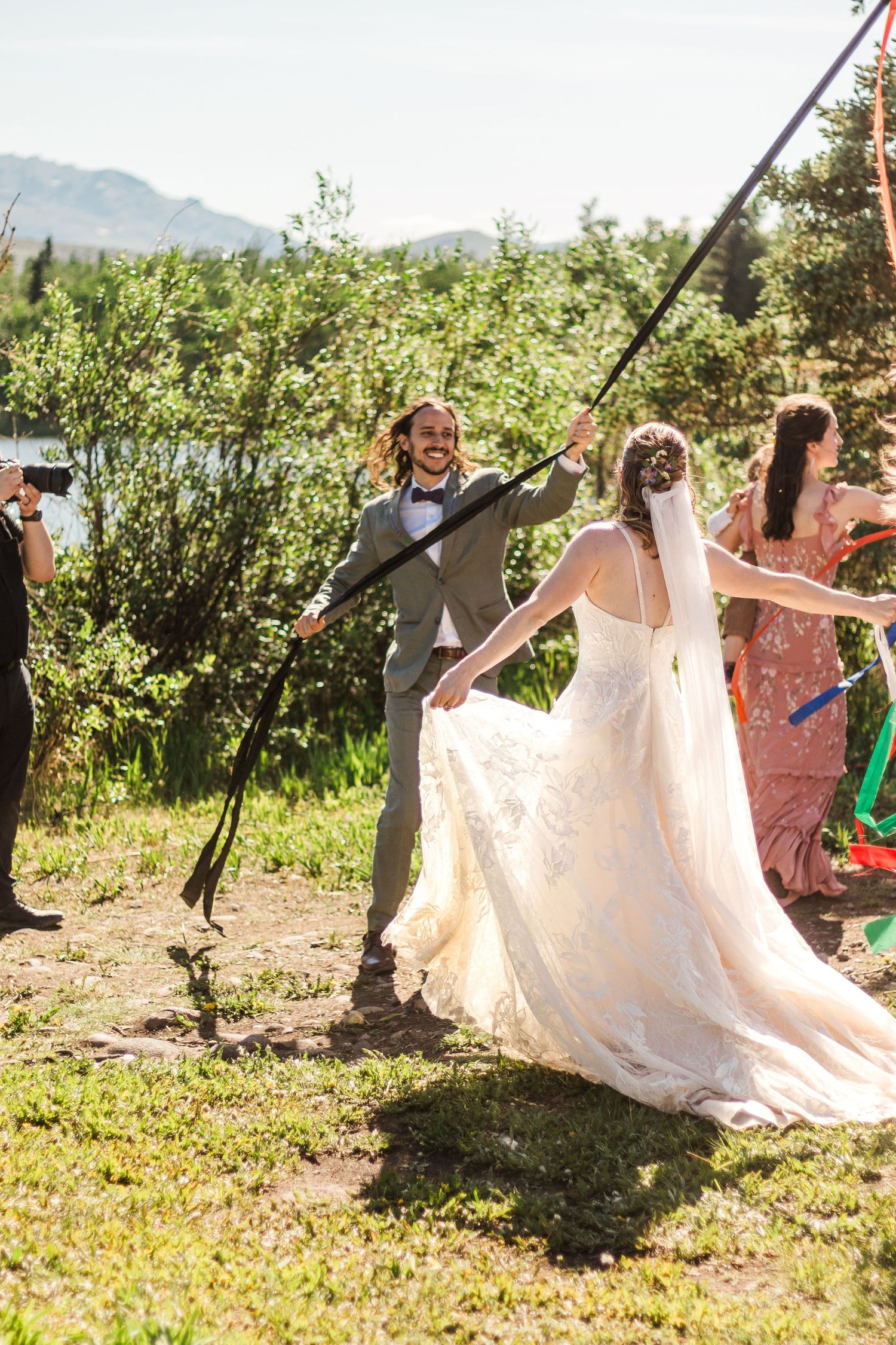 Celebration with wedding attire and joyful dancing by a lakeside mountain setting.