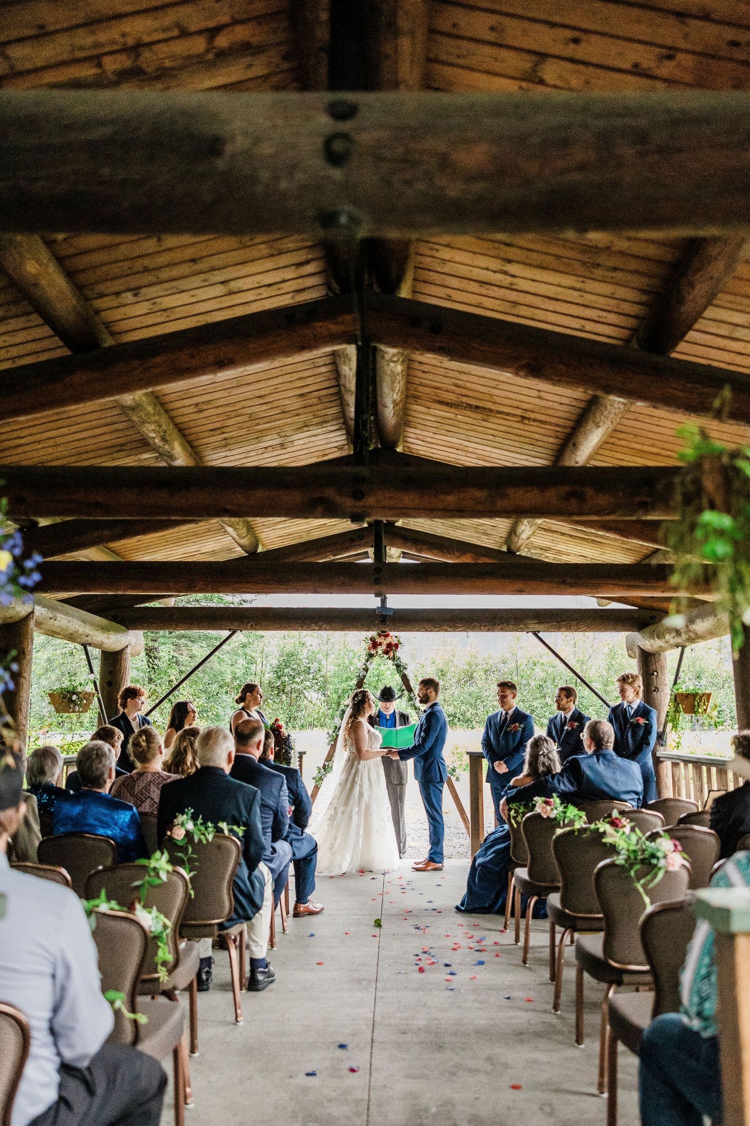 Wedding ceremony setup under a rustic wooden pavilion with rows of chairs and floral decorations.