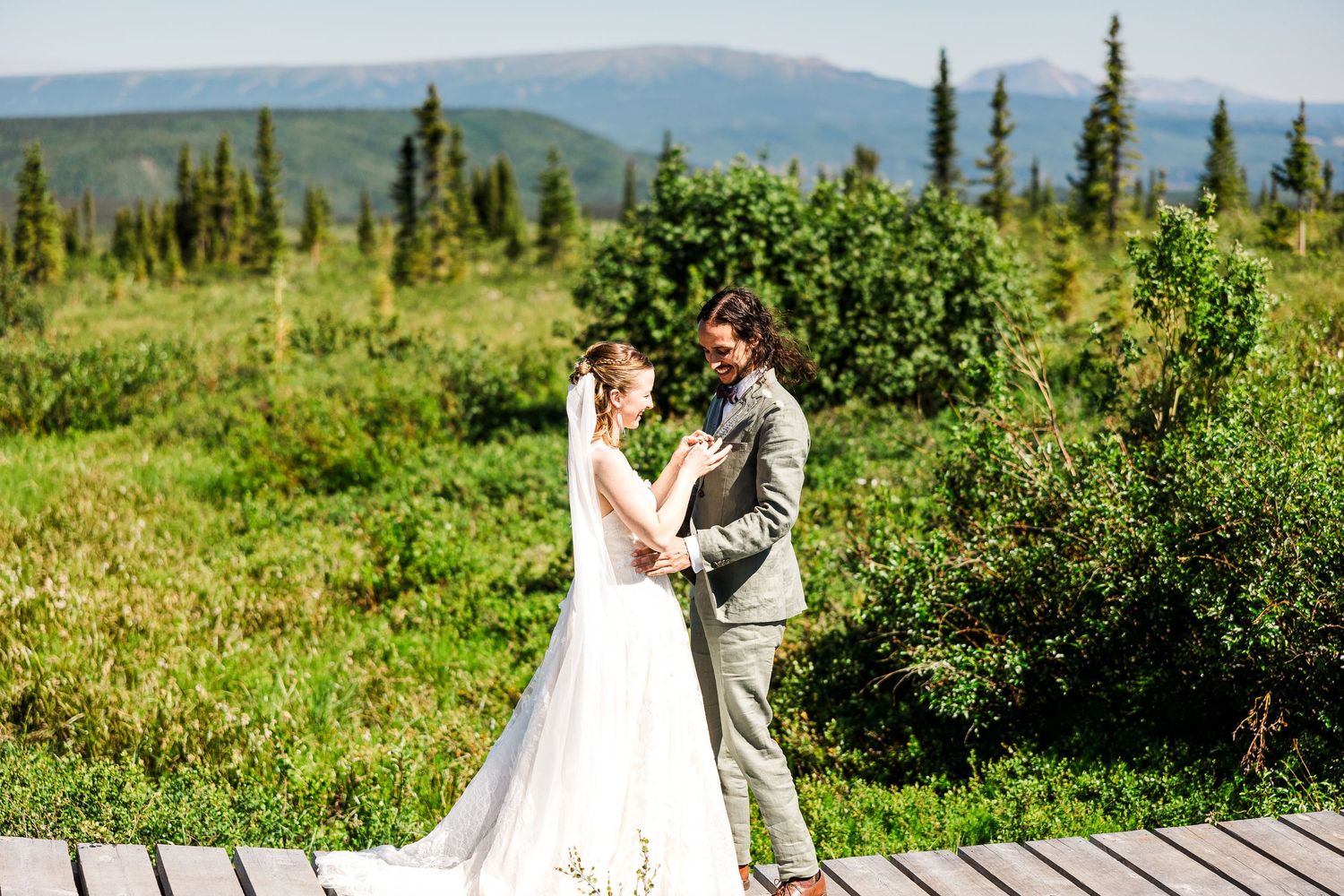 Couple shares romantic moment on wooden deck with mountain range backdrop.