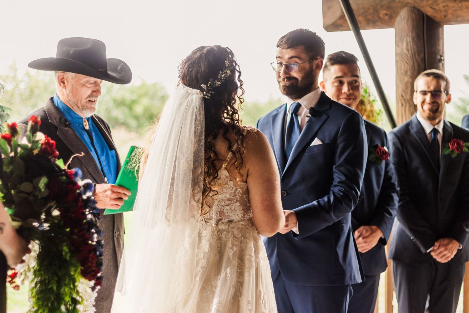 Wedding ceremony under a covered outdoor venue with officiant and wedding party.
