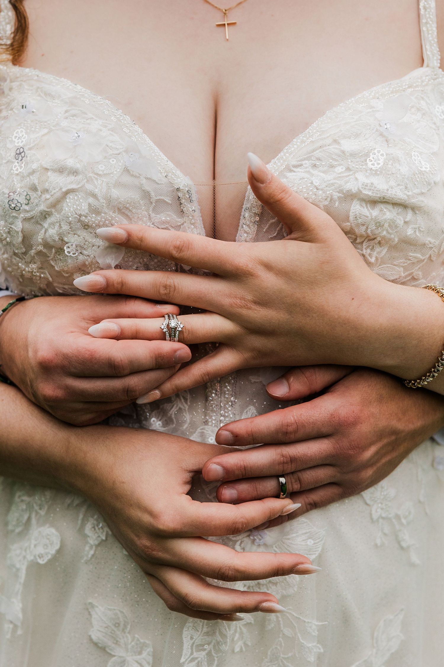 Close up of hands with wedding rings against white lace wedding dress bodice.