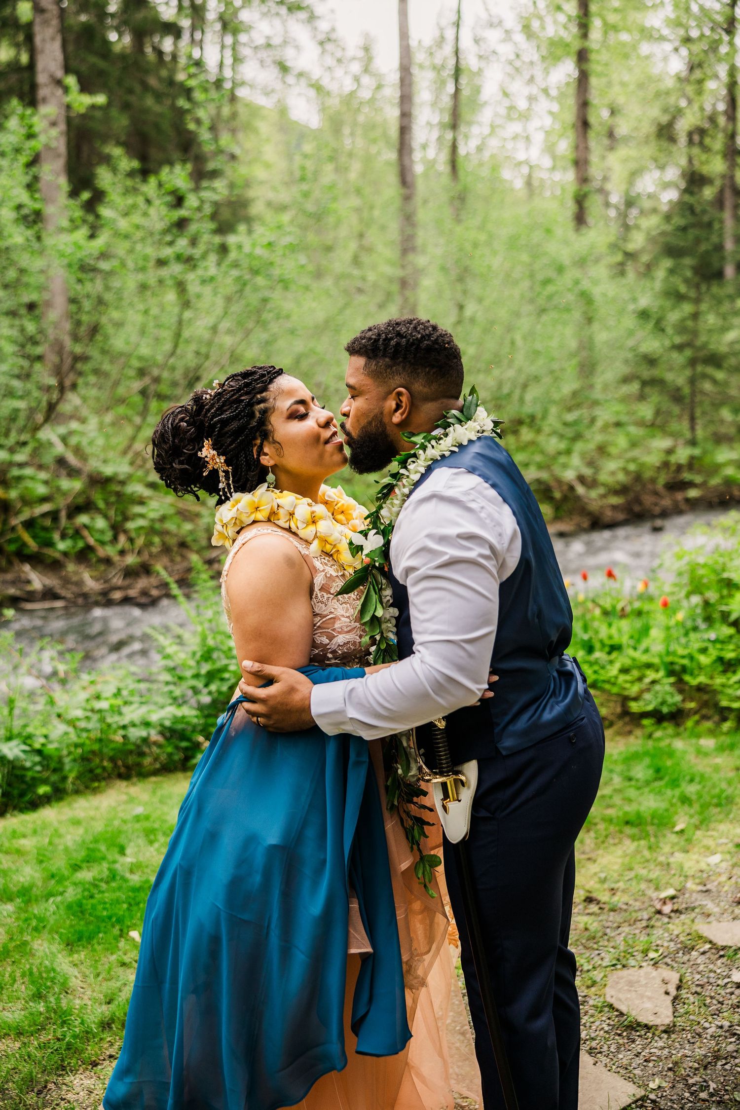 A tender embrace between a couple in wedding attire surrounded by green forest scenery.
