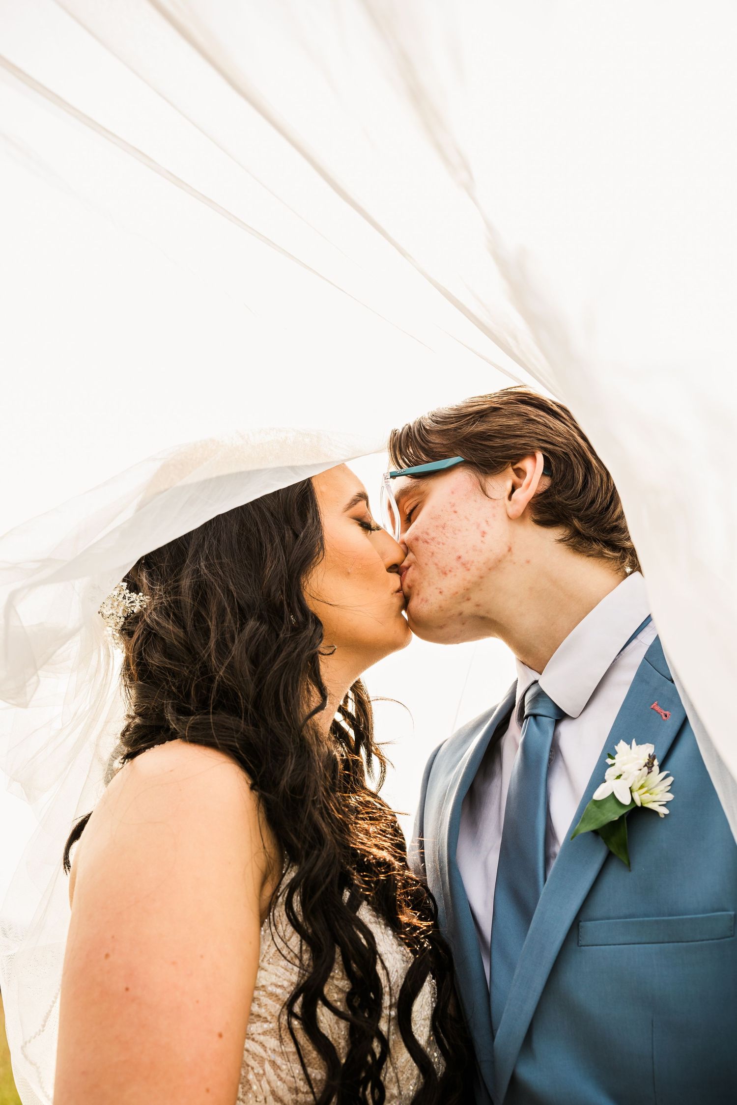 Wedding couple shares romantic kiss under flowing white veil.