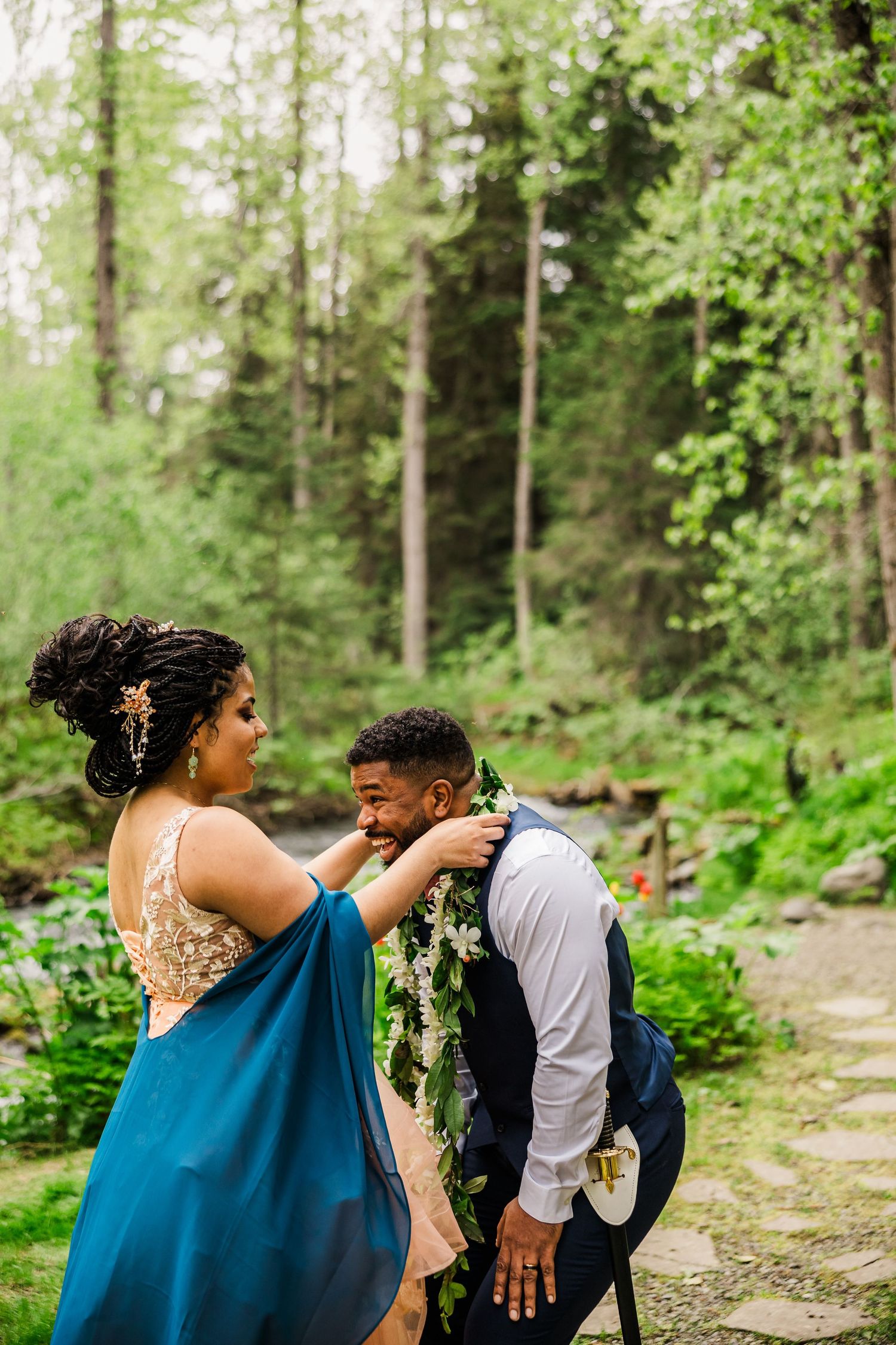 A couple in formal attire sharing an intimate moment in a lush forest setting during a wedding photoshoot.