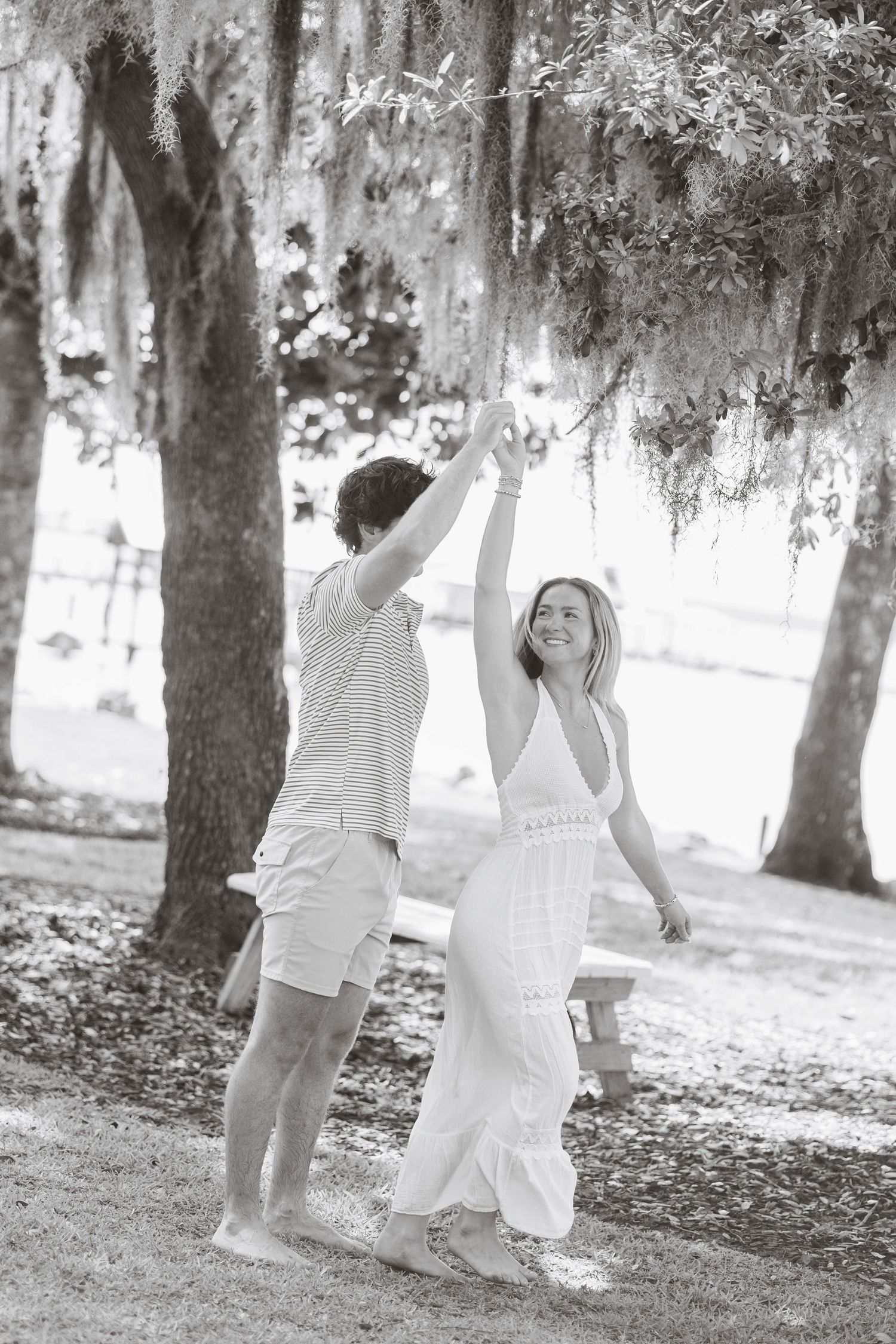 Black and white photo of a couple dancing under Spanish moss-draped trees outdoors.
