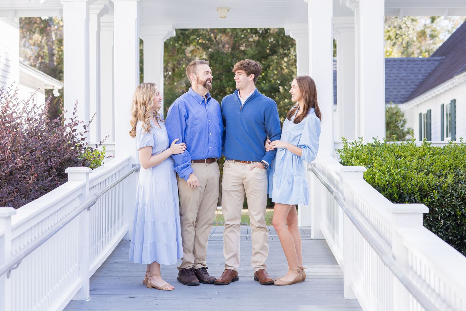 Two young adult couples posing together on a white columned porch in coordinating blue and tan outfits.